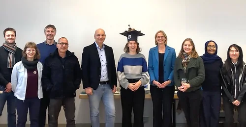 A group foto of smiling people, featuring Dr. Veronika Döpper with freshly earned and decorated mortar board in the center, her supervisors, some Cosmic Sense colleagues and more guests