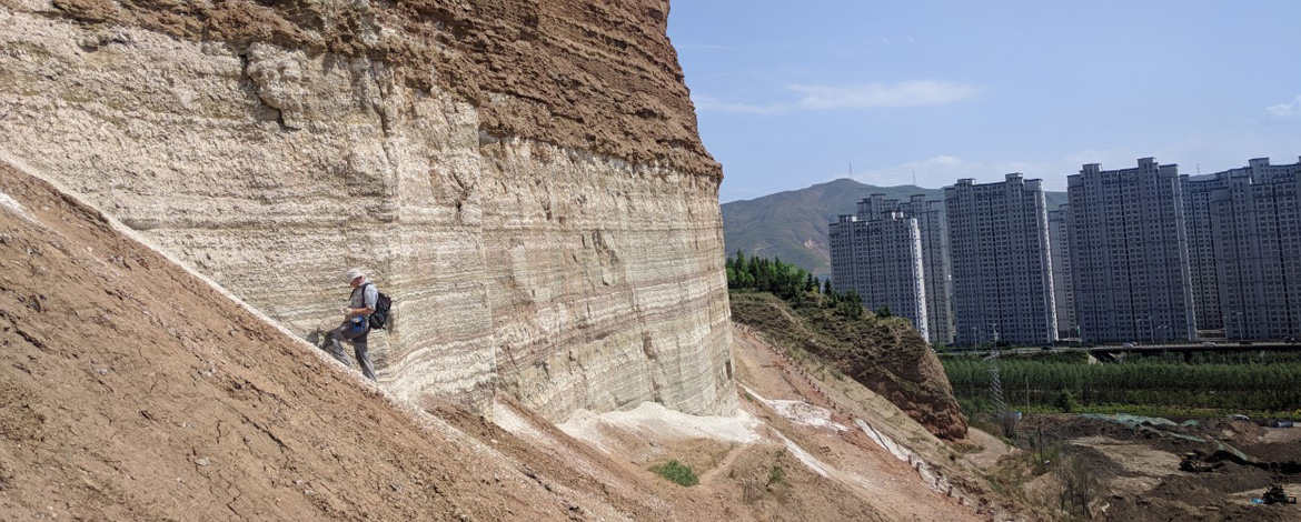 Geologist examines 42-million-year-old salt lakes to reconstruct the development of monsoons - in the background there are highrises of Xining City, China - 