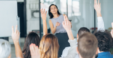 Rückansicht einer Gruppe von Leuten, die in einem Seminar die Arme heben, um eine Frage zu stellen